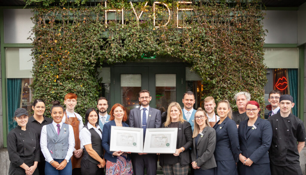 HYDE Bar Team Holding Awards Outside the Venue – A large group of hospitality staff and management from HYDE Bar pose proudly outside their greenery-covered entrance, holding framed awards. The "HYDE" sign is visible above the entrance, creating a celebratory and professional atmosphere.