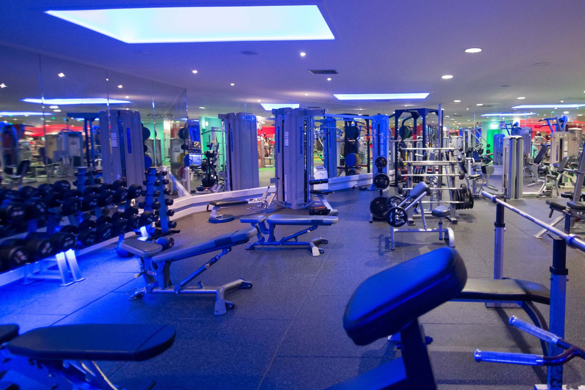 Active 24 Fitness Gym. A Modern Gym with Fitness Equipment – A spacious gym with various workout machines, weights, and benches, illuminated by cool blue lighting and mirrored walls.
