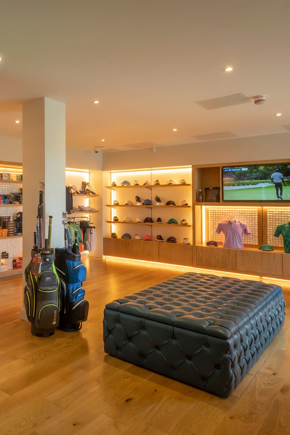 Galway Bay Golf Pro Shop Interior – A well-lit golf shop with neatly displayed caps, shirts, and golf accessories, along with a television screen showing a golf tournament, and golf bags arranged in the foreground.