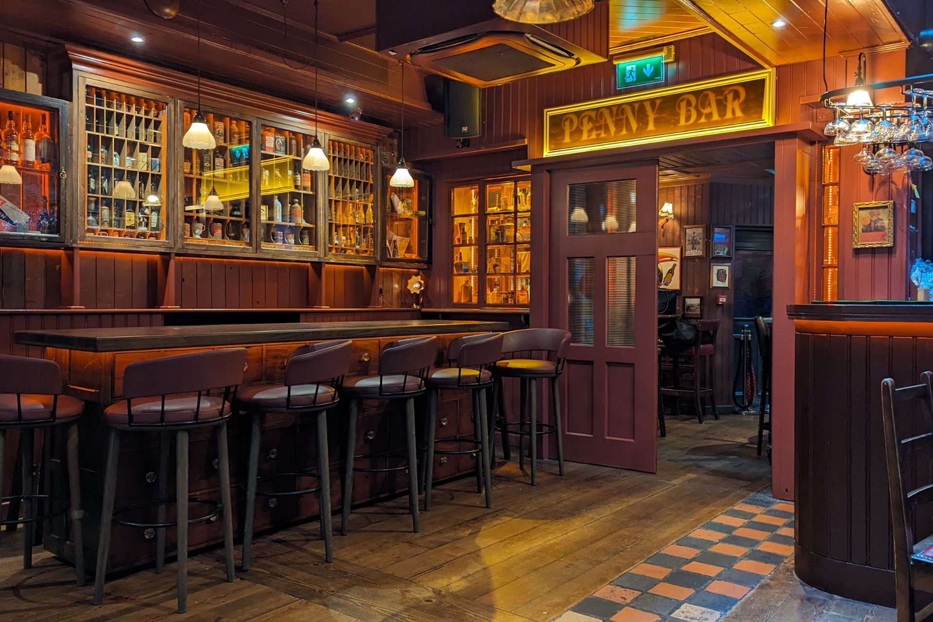 Traditional Irish Pub Interior – Penny Bar – A cosy, Irish pub with dark wooden furnishings, a well-stocked bar, warm lighting, and a sign reading "PENNY BAR" above the entrance.
