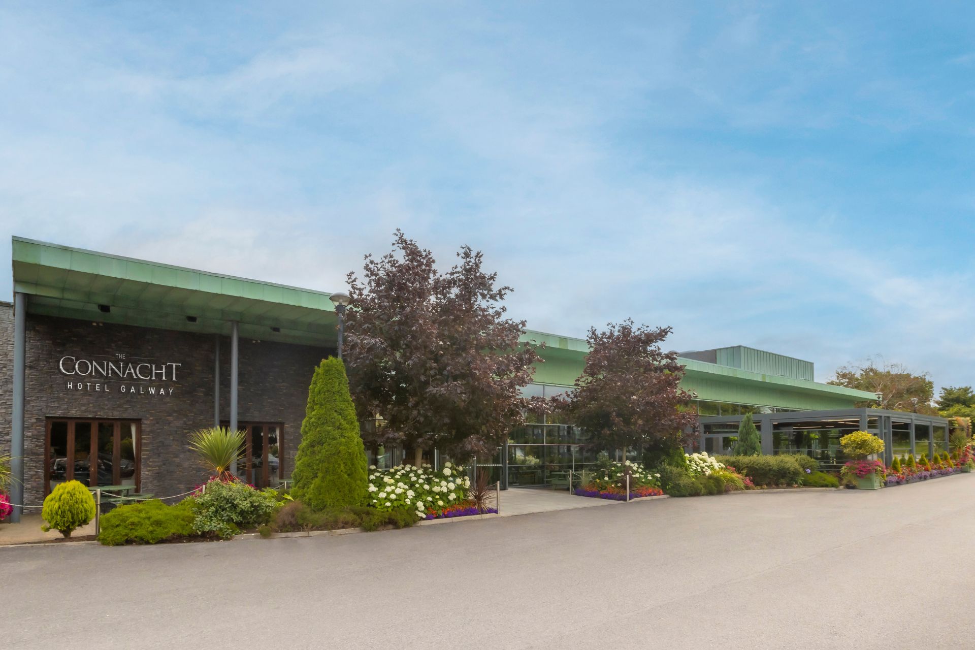 Exterior of The Connacht Hotel in Galway – A modern, welcoming hotel with a green roof, stone facade, and lush landscaping at the entrance, creating a warm and inviting atmosphere.