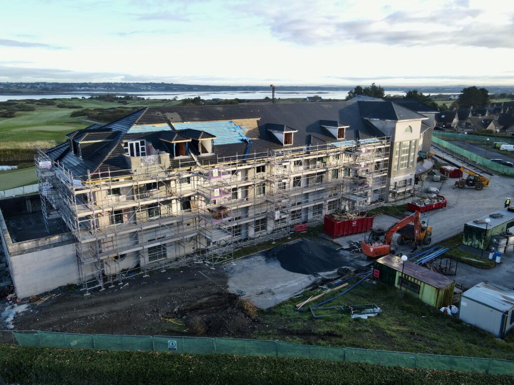 Close-Up of Hotel Under Construction – A detailed image of a hotel building in the midst of construction, with scaffolding, construction equipment, and workers actively engaged in the development process, set against a scenic waterfront backdrop.