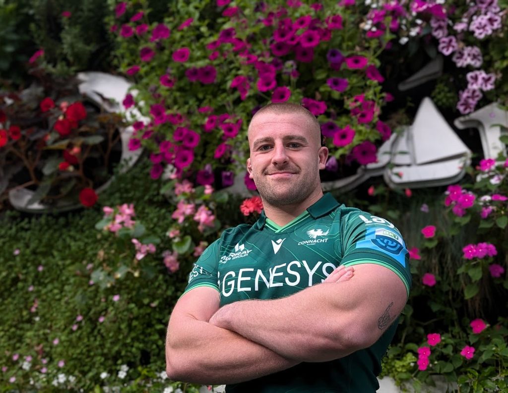 Connacht Rugby Player Posing in Front of a Floral Wall – A Connacht Rugby player stands confidently with arms crossed, wearing a green team jersey, against a lush wall of vibrant flowers. His strong stance and focused expression reflect team spirit and determination.