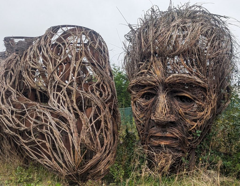 Woven Wooden Sculpture of a Face and Heart – A striking outdoor installation featuring an intricately woven wooden face sculpture alongside a similarly crafted heart, blending natural materials with artistic expression.