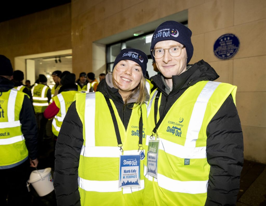 COPE Galway Sleep Out Volunteers – Two volunteers dressed in high-visibility vests and COPE Galway beanies smile at the camera during the Sleep Out event, raising awareness for homelessness.