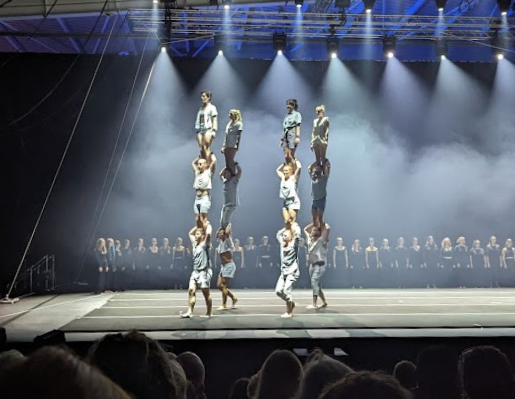 Acrobatic Performance at Galway International Arts Festival – A dramatic stage performance features acrobats balancing in high formations under theatrical lighting, with a choir in the background, creating an impressive visual display.